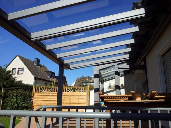 Moderne Terrassenüberdachung aus Glas und Metall an einem Einfamilienhaus im Garten.