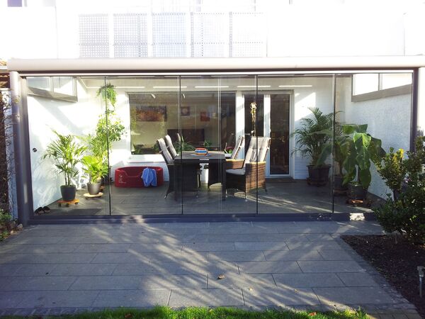 Moderner Wintergarten mit Glasfront, Gartenmöbeln und vielen grünen Zimmerpflanzen.