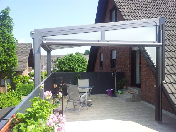 Große Terrasse mit moderner Überdachung, Gartenmöbeln und Blumen an einem Wohnhaus.