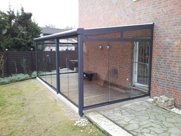 Moderner Wintergarten aus Glas mit Aluminiumrahmen an einem Einfamilienhaus im Garten.