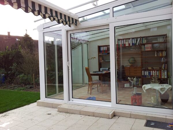 Moderner Wintergarten mit großen Glasfronten, Blick ins helle Homeoffice mit Regalen.